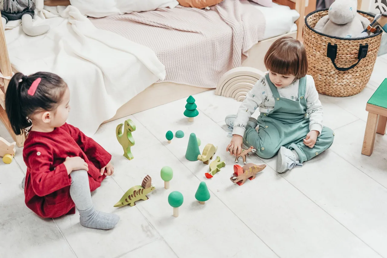 Two young children playing with wooden toys in a bedroom
